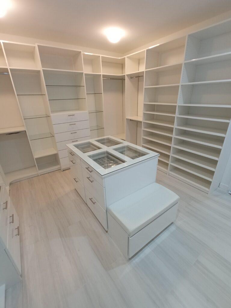 Completed custom white walk-in closet with shelving, drawers, and a center island